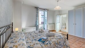 Un dormitorio con cama, mesita de noche, lámpara, ventana con cortinas y vistas al exterior.