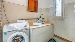 Un área de lavandería compacta con lavadora, un armario de madera, una ventana y un lavamanos pequeño con productos de limpieza.
