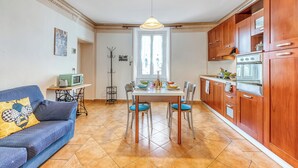Una cocina compacta con armarios de madera, una mesa de comedor con sillas, un sofá con cojines estampados y una máquina de coser en un rincón.
