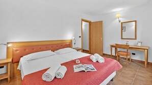Una camera d'albergo con un letto, una scrivania, una sedia, una lampada e uno specchio.