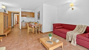 Un soggiorno con un divano rosso, un tavolino da caffè con una pianta, una zona pranzo con tavolo e sedie, e una cucina sullo sfondo.
