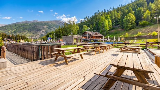 Un pontile in legno con tavoli da picnic, un piccolo edificio e montagne sullo sfondo.