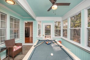 A pool table in a room with teal walls, a ceiling fan, and a door leading to another room.