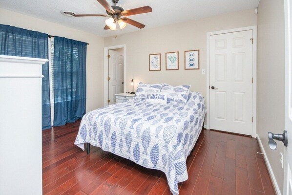 A bedroom with a bed, a ceiling fan, a door, and a window with curtains.