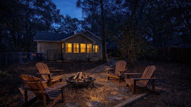 A cabin with a fire pit and four Adirondack chairs in a wooded area. - Coastal Comfort- Intracoastal Waterway Escape (Murrells Inlet)