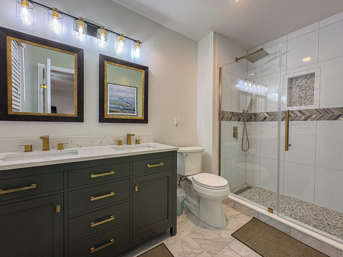 Een moderne badkamer met een donkere wastafel, een wit toilet en een douche met glazen wanden.