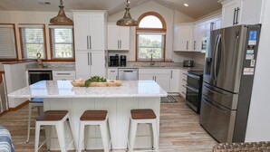 Una cucina moderna con mobili bianchi, una grande isola con sgabelli, elettrodomestici in acciaio inossidabile e un lampadario a sospensione.