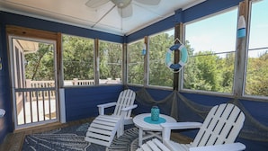 Una veranda con ampie finestre, poltrone Adirondack bianche, un tavolino e un tappeto decorato.
