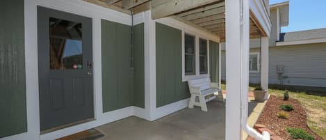 A covered porch with a bench, a door, and a small garden area.