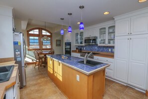 A kitchen with a central island, white cabinets, and blue pendant lights. - Seven Seas - 4 BR Oceanfront Home w/Private Pool & Ocean Views (Southern Shores)