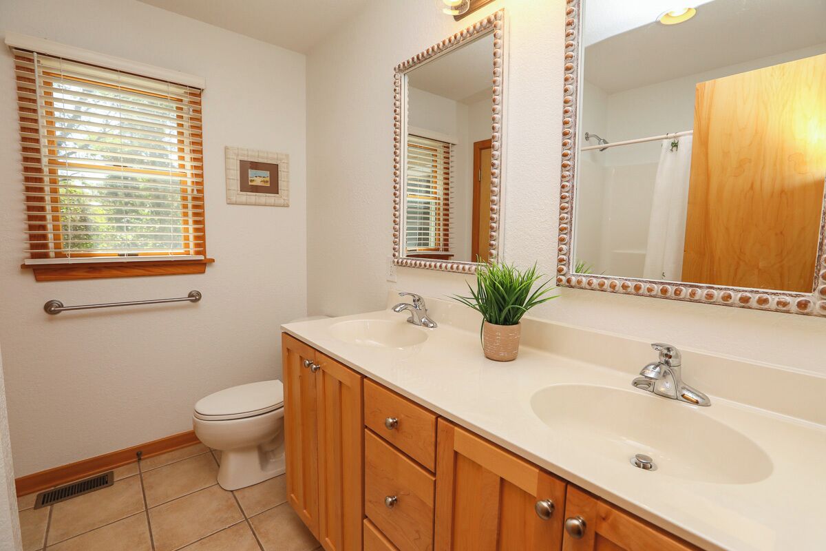 A bathroom with a white toilet, wooden vanity with two sinks, and a large mirror with a decorative frame.