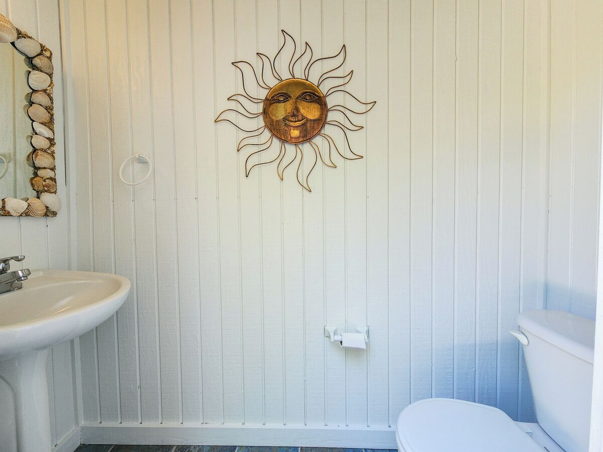 A bathroom with a white sink, toilet, and a decorative sun wall art piece.