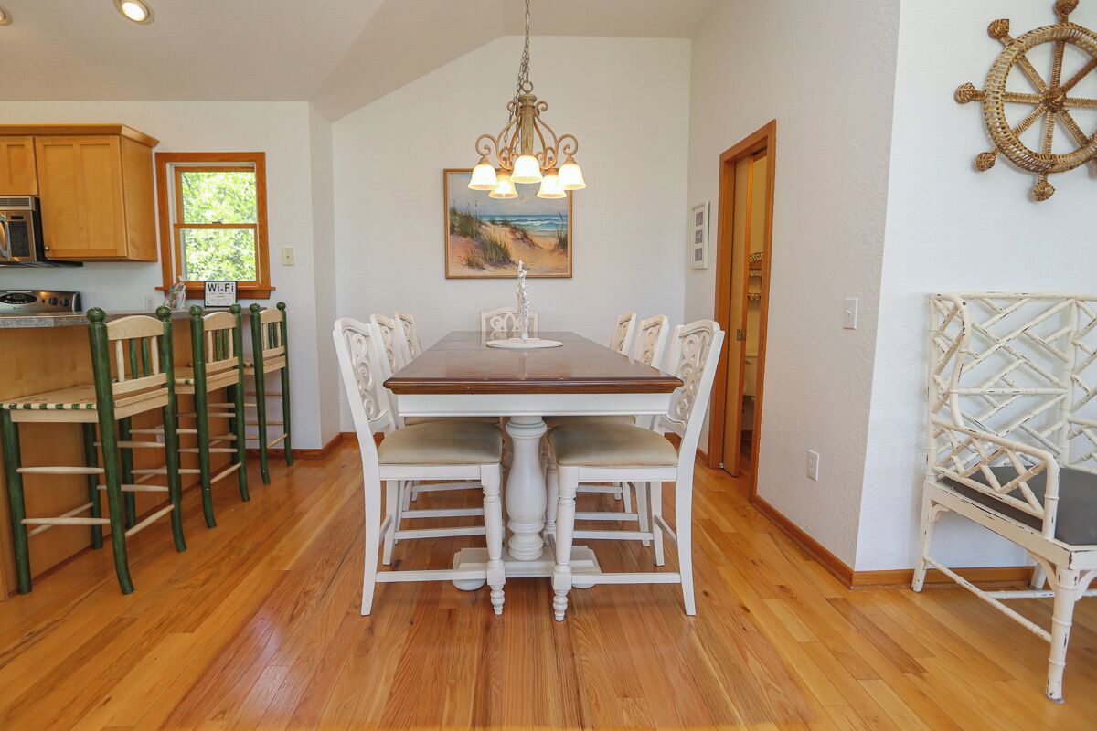 A dining area with a wooden table and chairs, a chandelier, and a nautical-themed wall decoration.