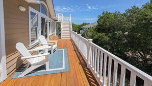 Eine Holzterrasse mit weißen Geländern, mehreren Adirondack-Stühlen und einer Treppe, die zu einer erhöhten Ebene führt.