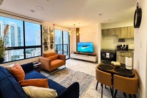 A modern living room with a sofa, a coffee table, a TV, and a dining area with chairs. - Modern Apartments at The Gray Prime Location (Panama City)