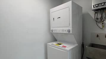 Une petite buanderie équipée d’un lave-linge et d’un sèche-linge, d’un évier et d’un chauffe-eau fixé au plafond.