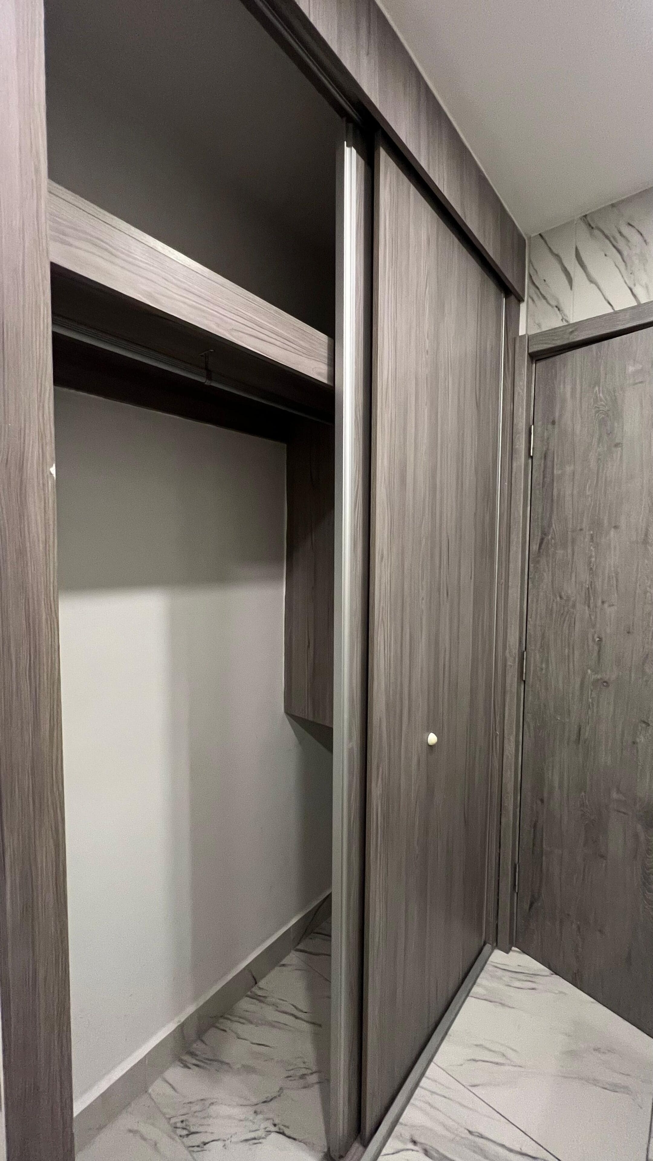 A modern closet with sliding doors, a marble floor, and a wooden ceiling.