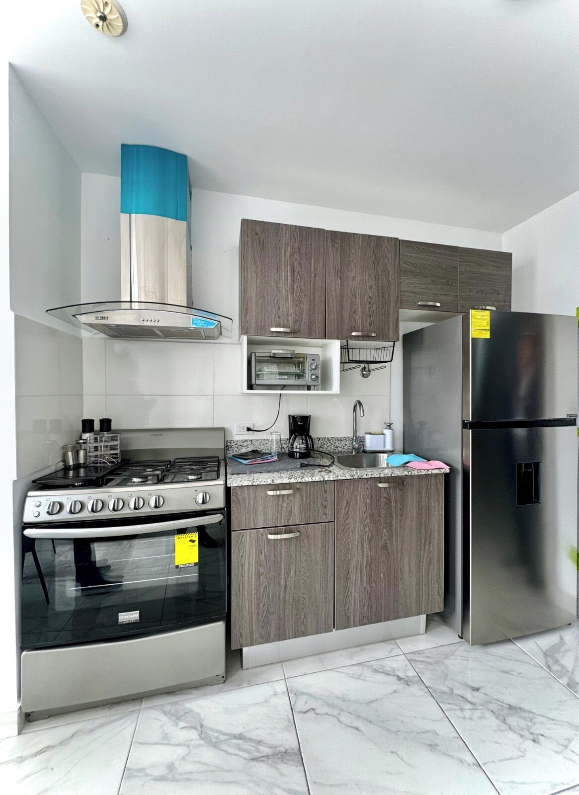 Una cocina moderna con estufa a gas, microondas, tostadora y refrigerador de acero inoxidable.