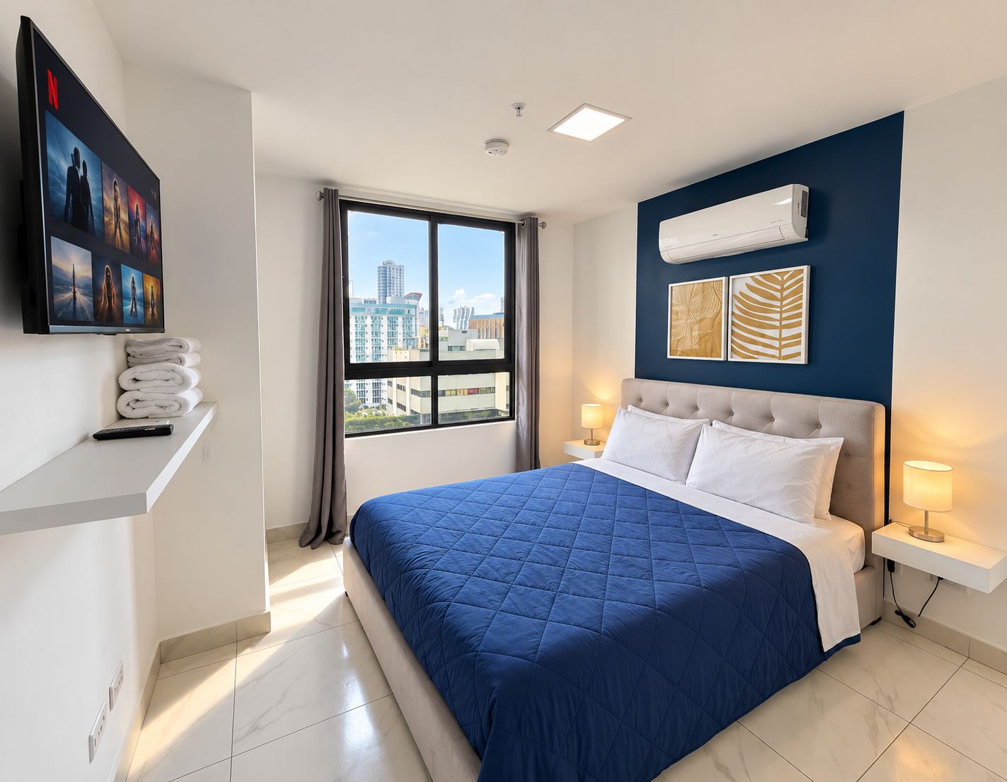 Ein Hotelzimmer mit Bett, Wandfernseher, Fenster mit Stadtblick und Klimaanlage.