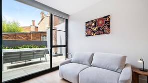 Ein modernes Wohnzimmer mit grauem Sofa, einem großen Fenster und einem farbenfrohen abstrakten Gemälde an der Wand.