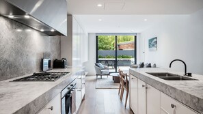 A modern kitchen with a large island, stainless steel appliances, and a view to an outdoor patio. - Stoneyard, Prahran (Prahran)