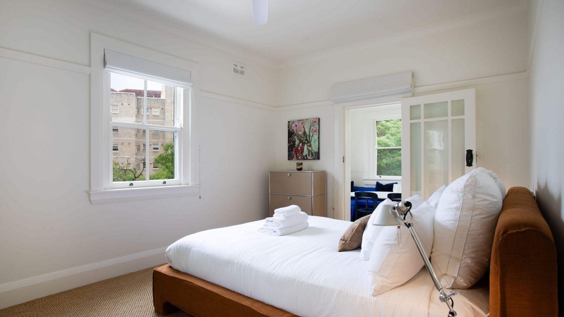 A bedroom with a bed, a bedside table, a lamp, a wardrobe, and a painting on the wall.