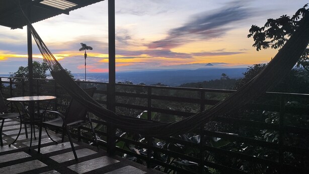 Une terrasse dotée d’un hamac, de chaises et d’une table, offrant une vue imprenable sur un paysage magnifique, notamment au coucher du soleil.