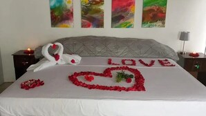 Un lit décoré de cygnes et de motifs en forme de cœur, un panneau «AMOUR» réalisé avec des pétales de rose, et des œuvres d’art colorées accrochées au mur.