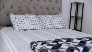 Ein ordentlich bezogenes Bett mit einem karierten Kissen und einer Decke mit geometrischem Muster.