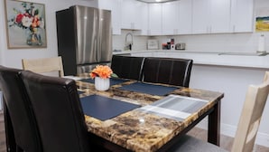 Eine moderne Küche mit weißen Schränken, einem Edelstahl-Kühlschrank und einem Essbereich mit Marmortisch und schwarzen Stühlen.