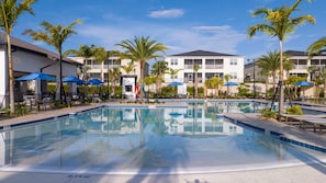 A swimming pool with lounge chairs and umbrellas, surrounded by palm trees and a building with balconies. - Family Villa Private Pool Spa Arcade Sleeps 22 (Davenport)