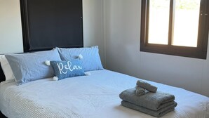 Una cama bien tendida con ropa de cama a rayas y una almohada que dice 'Relax'.