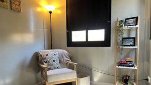 Habitación de esquina con una silla de madera, una lámpara de pie, una estantería y una ventana con persianas.
