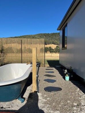 A bathtub outside a building with a view of a fence and hills in the background.