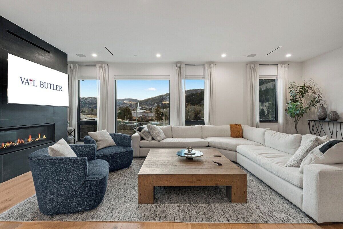 A modern living room with a fireplace, a sectional sofa, a coffee table, and large windows offering a view of a cityscape.