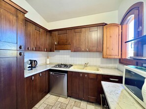 A kitchen with dark wooden cabinets, a stainless steel dishwasher, a gas stove, and a microwave. - "Family        House" (Bari Sardo)