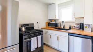 Una cocina compacta con gabinetes blancos, un refrigerador de acero inoxidable, una estufa negra y un lavavajillas.