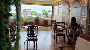 A spacious indoor area with multiple wooden tables and chairs, large windows offering views of the outside, and potted plants adding greenery. - Hotel Yagua Iquitos (Belen)