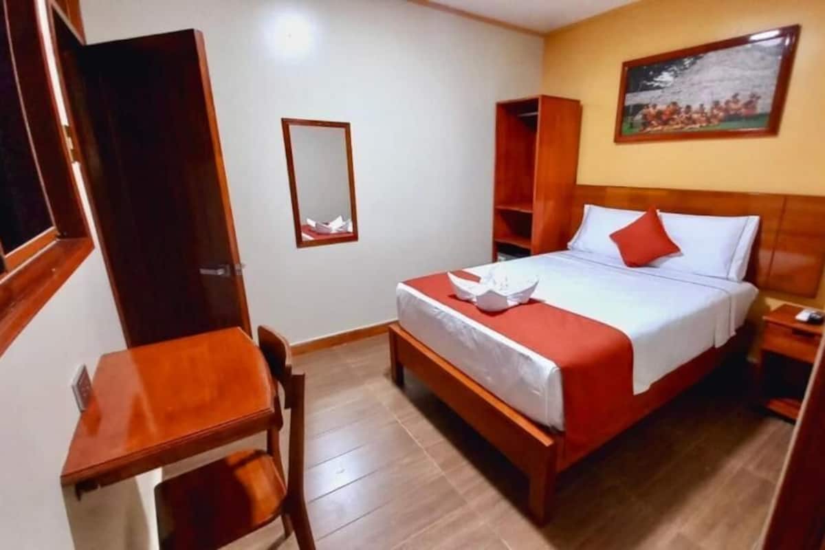 Une chambre d’hôtel avec un lit, un bureau, une chaise, une armoire et un tableau au mur.