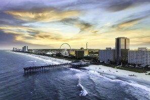 A coastal cityscape with a pier extending into the ocean, a beach, and a Ferris wheel in the background. - Beachside Townhouse Walk to Ocean/wheel &boardwalk (Myrtle Beach)
