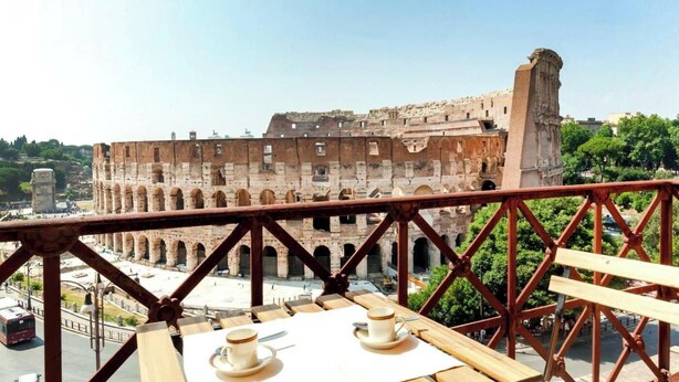 Een balkon met uitzicht op het Colosseum en een tafel met een kopje en schoteltje.