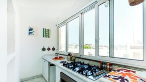 Een kleine keuken met een gasfornuis, oven en een raam met uitzicht op een stadsgezicht.