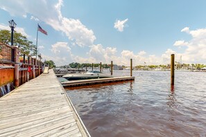 A wooden dock extending into calm water with boats docked nearby, a clear sky, and an American flag. - Lakeview condo with private patio, pool, close to beach & golf (North Myrtle Beach)