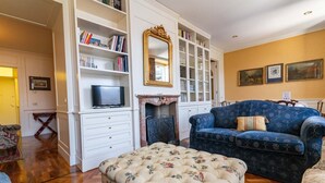 A living room with a sofa, ottoman, fireplace, bookshelves, and a television. - Casa Orta apartment with lake view (Orta San Giulio)