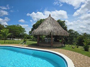 Una piscina con un pabellón de techo de paja y sillas.