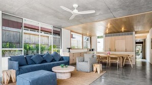 Een moderne woonkamer met een blauwe bank, een ronde salontafel en een eethoek met een houten tafel en stoelen.