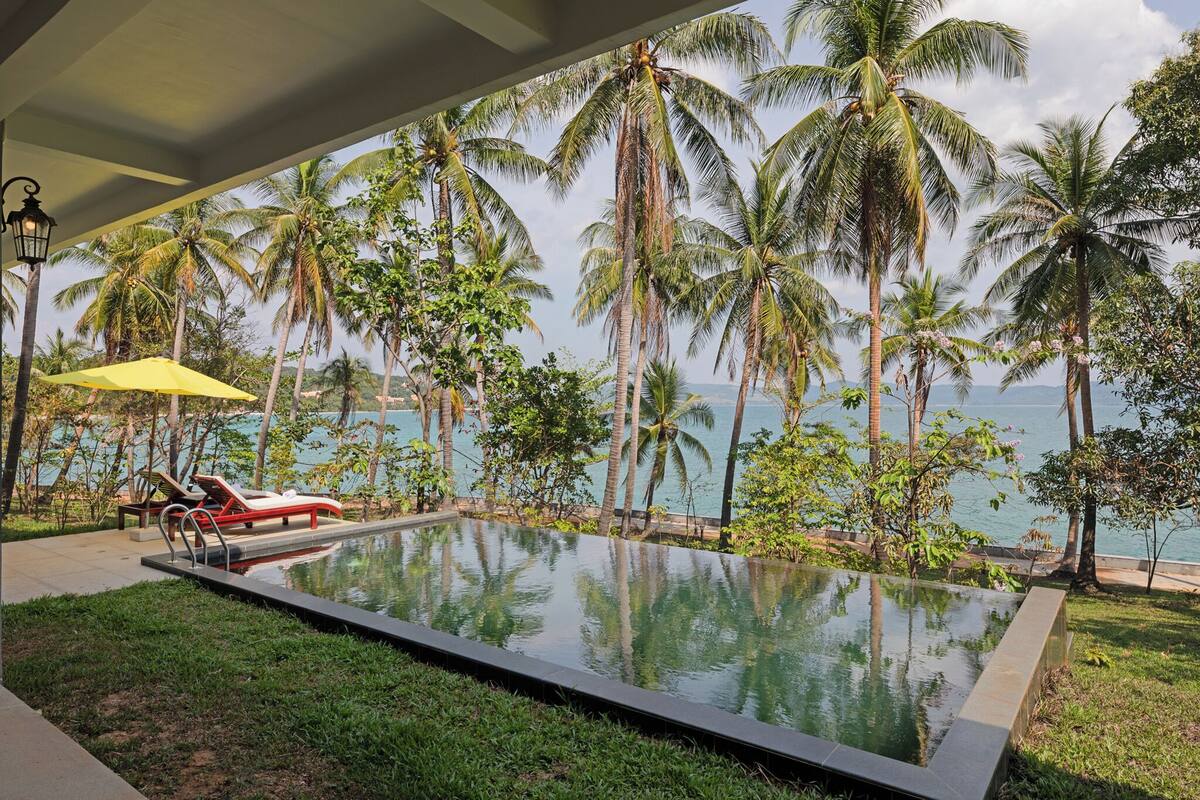 A pool with a view of the sea, surrounded by palm trees.