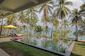 A swimming pool with a view of the sea, surrounded by palm trees and a yellow umbrella.