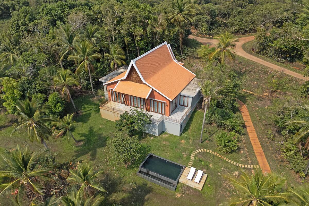 A house with a sloped roof, surrounded by lush greenery and a small pool.