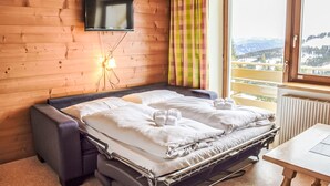 A cozy room with a bed, a TV mounted on the wall, and a window with a view of the mountains. - Katschberg 26 by Interhome (Sankt Michael im Lungau)